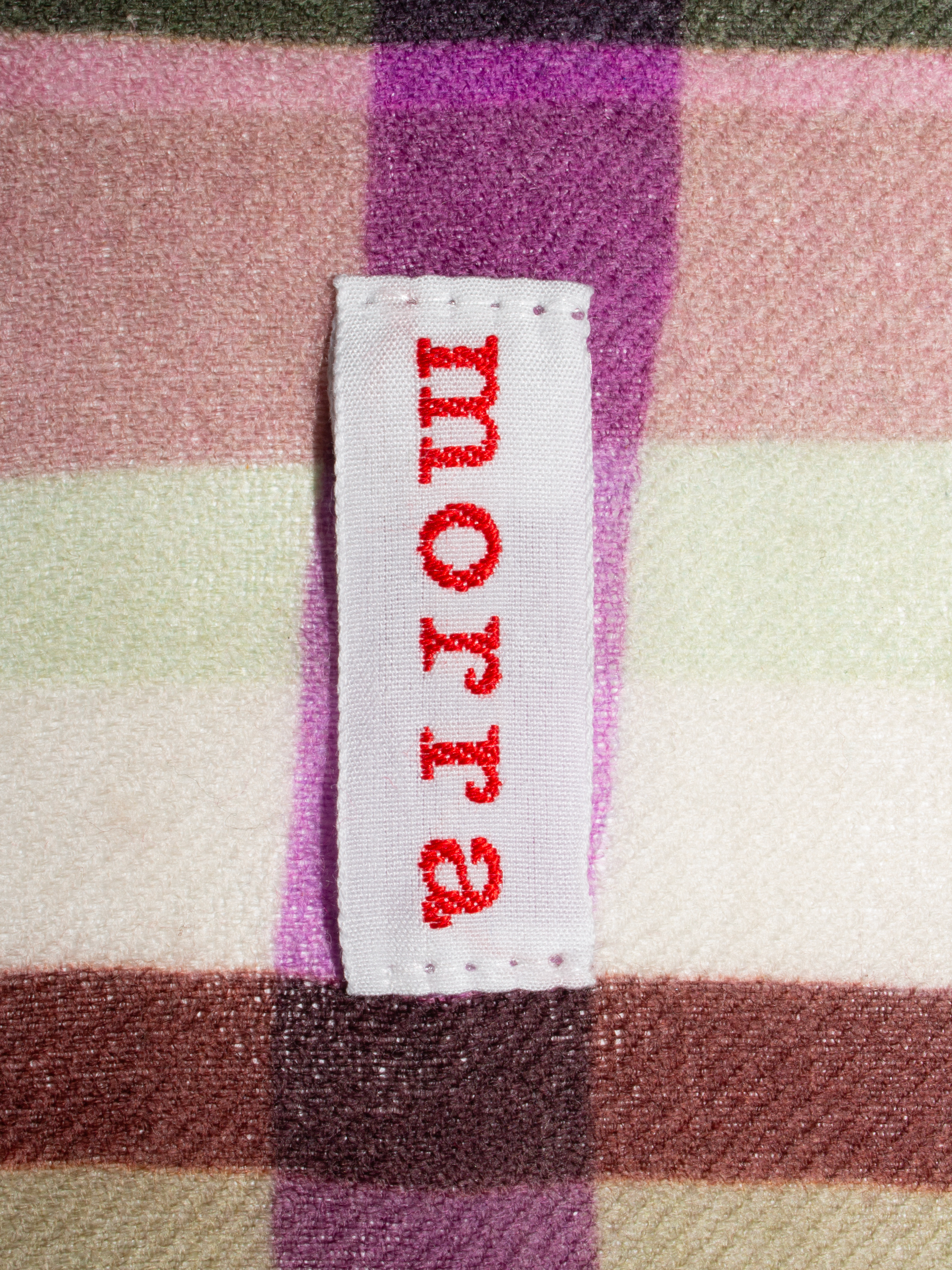 A close-up of a clothing label on a checkered wool scarf.
