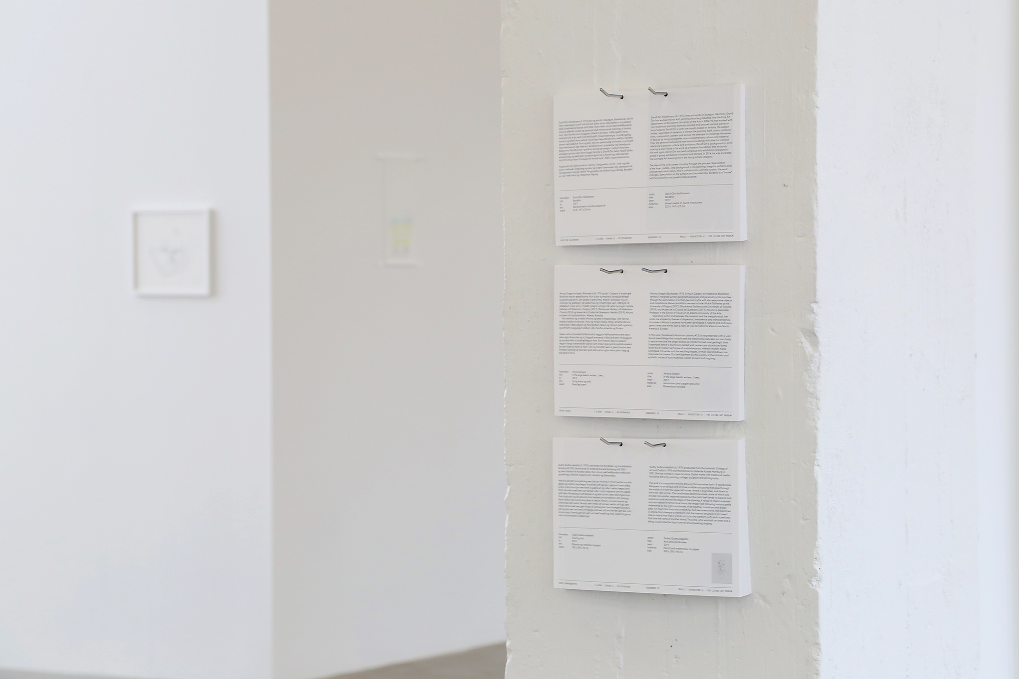 Three stacks of object labels hang on a white column in a gallery.