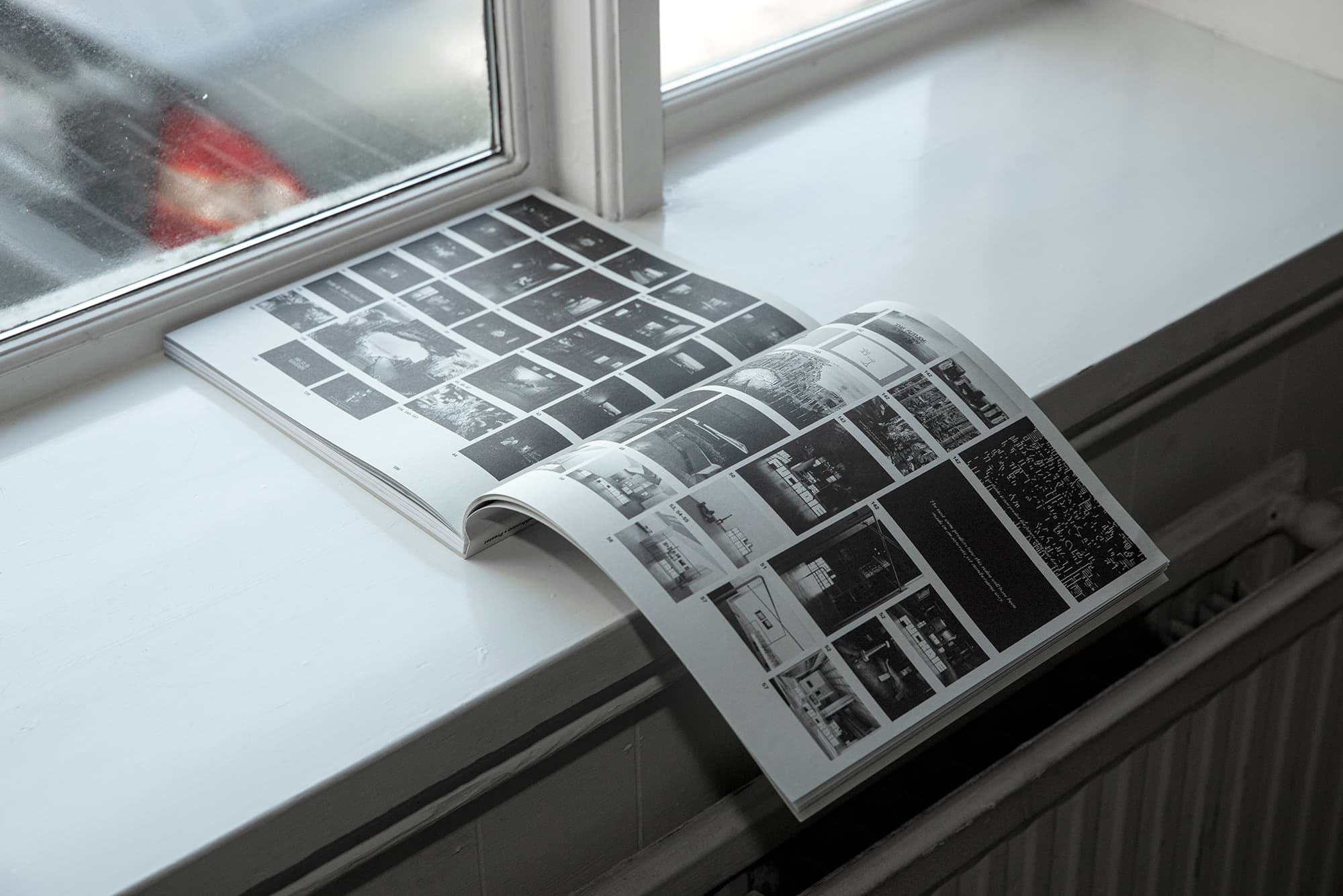 An open book sitting on a window sill. The book spread shows a mosiac of multiple black and white images.